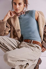 Worn-in blue tee layered under a shearling-lined jacket and silk neck scarf