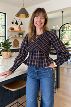 A woman wearing a navy and brown plaid wrap-style long-sleeve top with blue jeans.